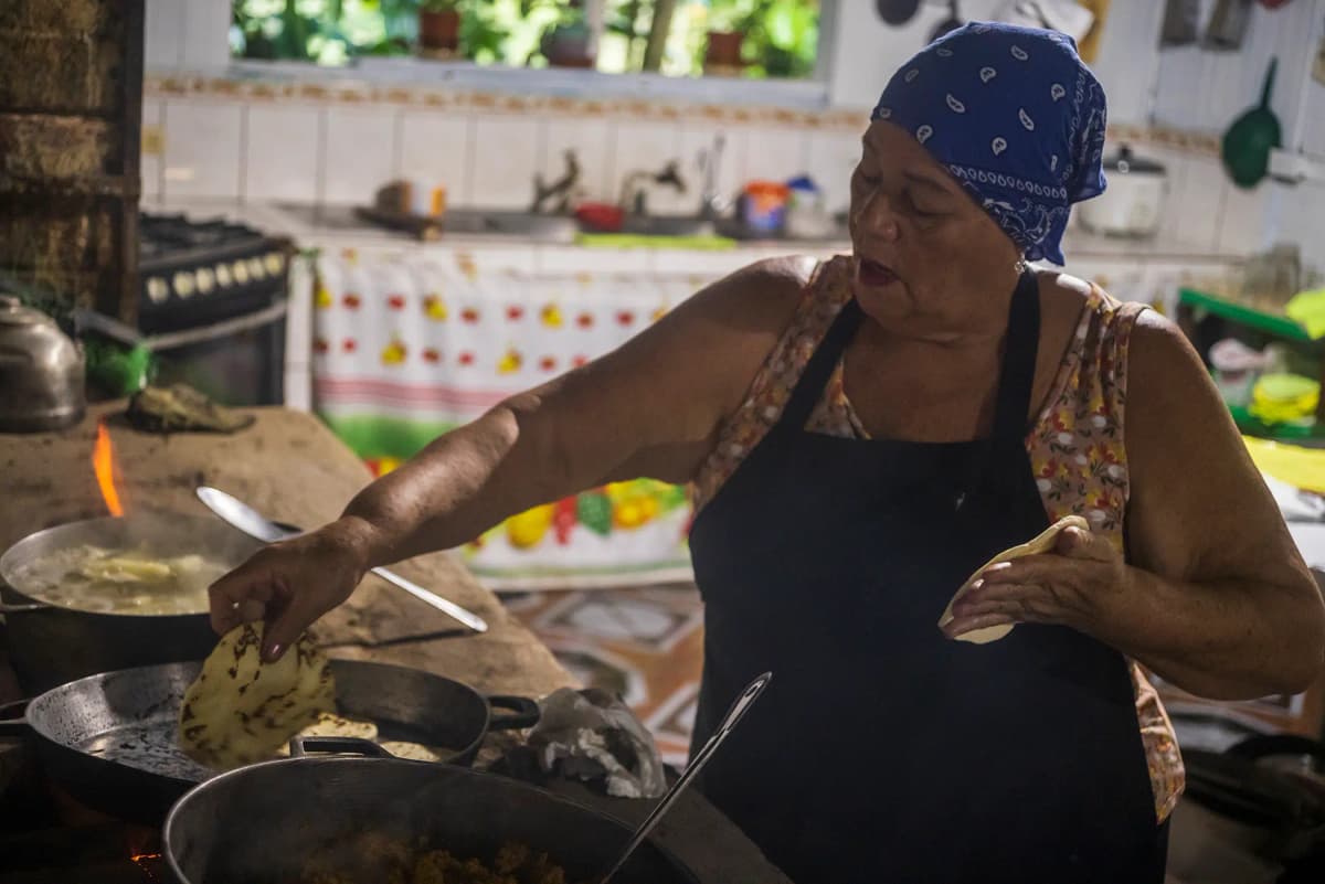 Traditional cook pressing and cooking handmade corn tortillas over a wood fire